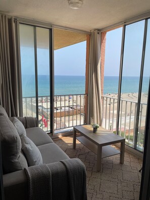 Ein Balkon mit Blick auf den Strand, einer Couch und einem kleinen Tisch.