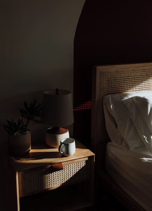 A neatly made bed with a headboard, a bedside table with a lamp, a potted plant, and a mug. - 3-bedroom house in El Prado, includes 2 bedroom casita on property. (El Prado)