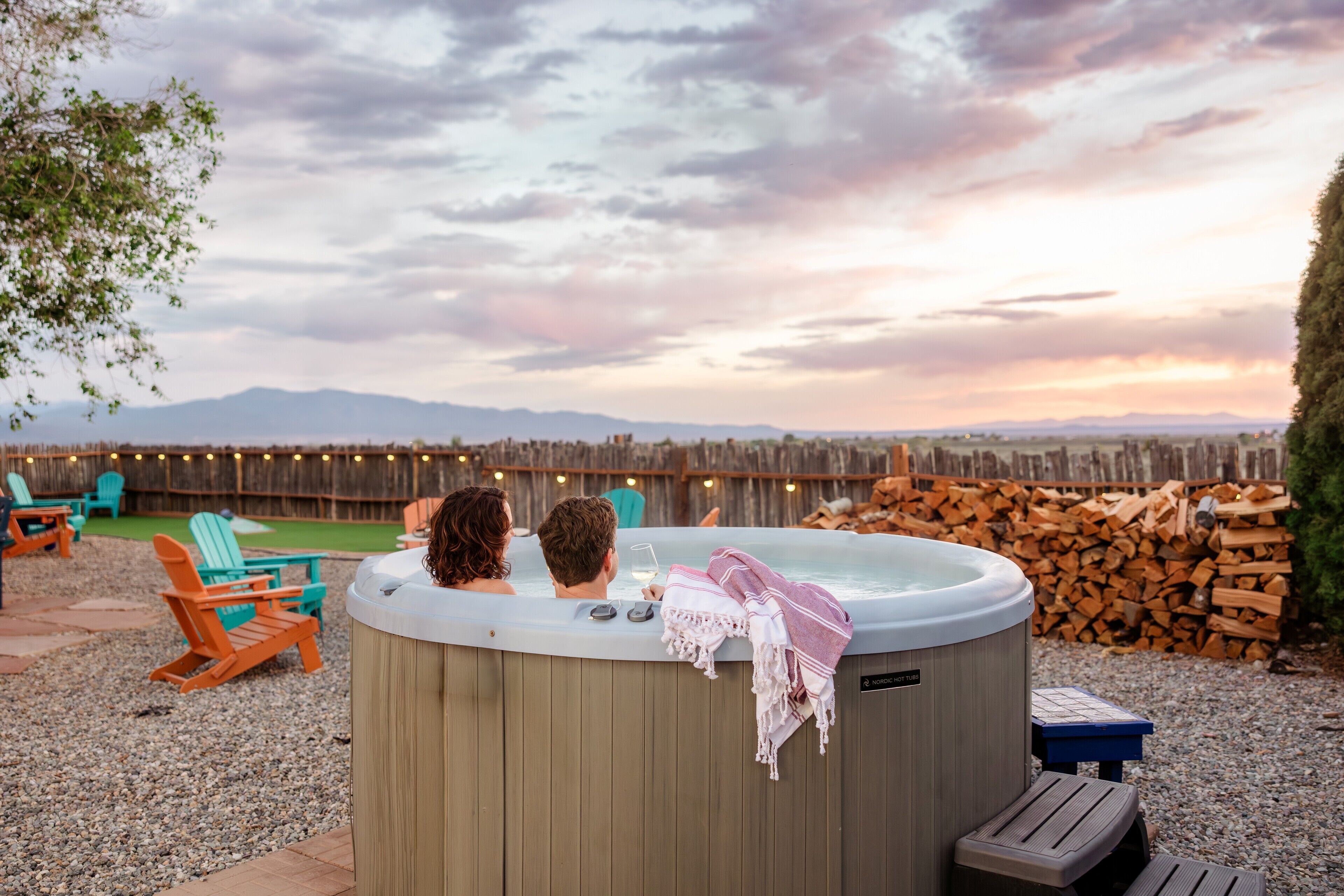 Un jacuzzi con dos personas adentro, rodeado de mobiliario exterior y una valla de madera.