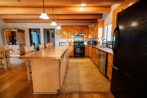 A kitchen with wooden cabinets, a central island, and a black refrigerator. - 5 King Rooms, Game Room, Hot Tub, Enclosed Yard, Views (El Prado)