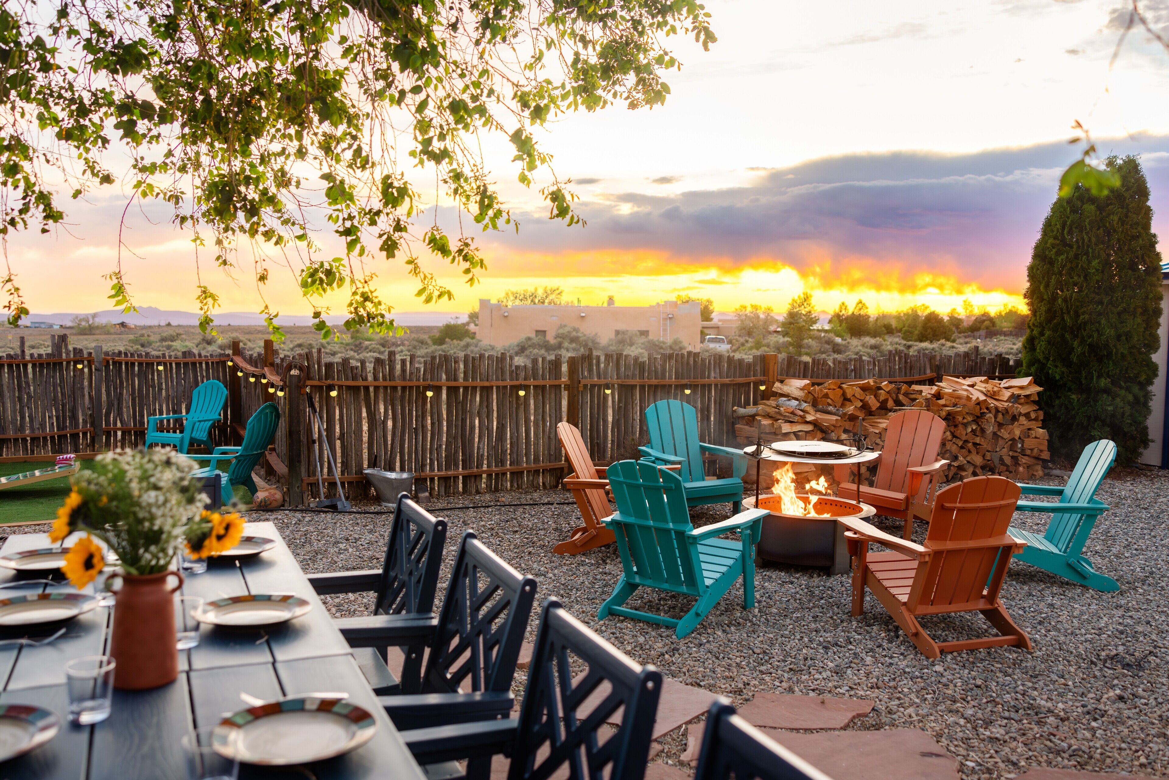 An outdoor seating area with Adirondack chairs, a fire pit, and a table set for dining.
