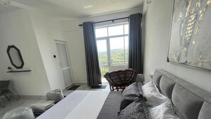 A bedroom with a large bed, a chair, a sofa, a window with curtains, and a painting on the wall. - Loft 123 - Kandy (Kandy)