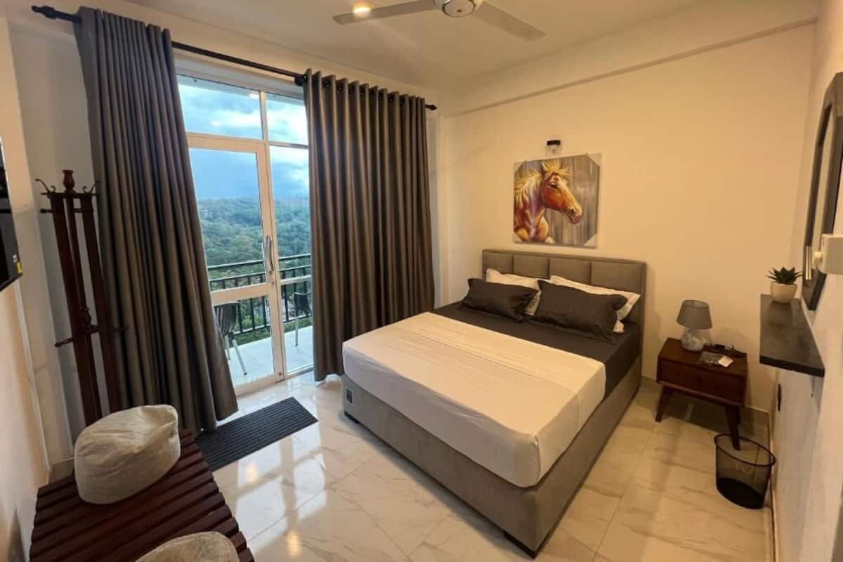Quarto com cama, ventoinha no teto, pintura, mesa de cabeceira e vista pela janela.