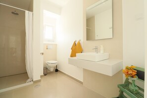 Et badeværelse med brusebad, toilet, vask og spejl.
