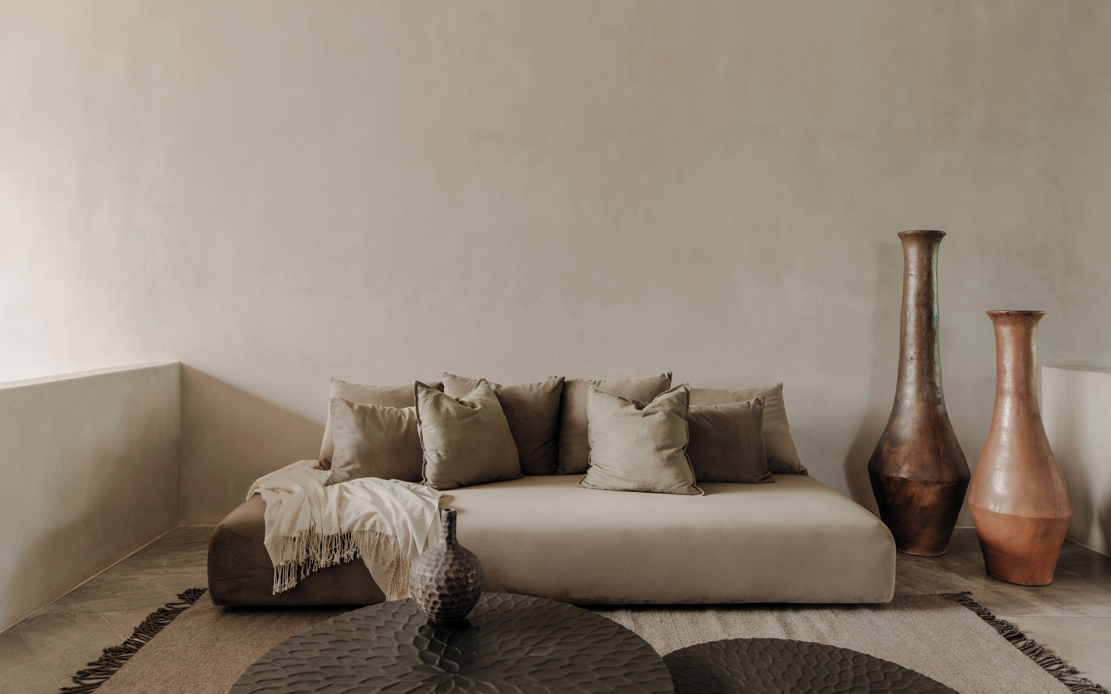 A corner room with a beige sofa, two vases, and a textured rug.