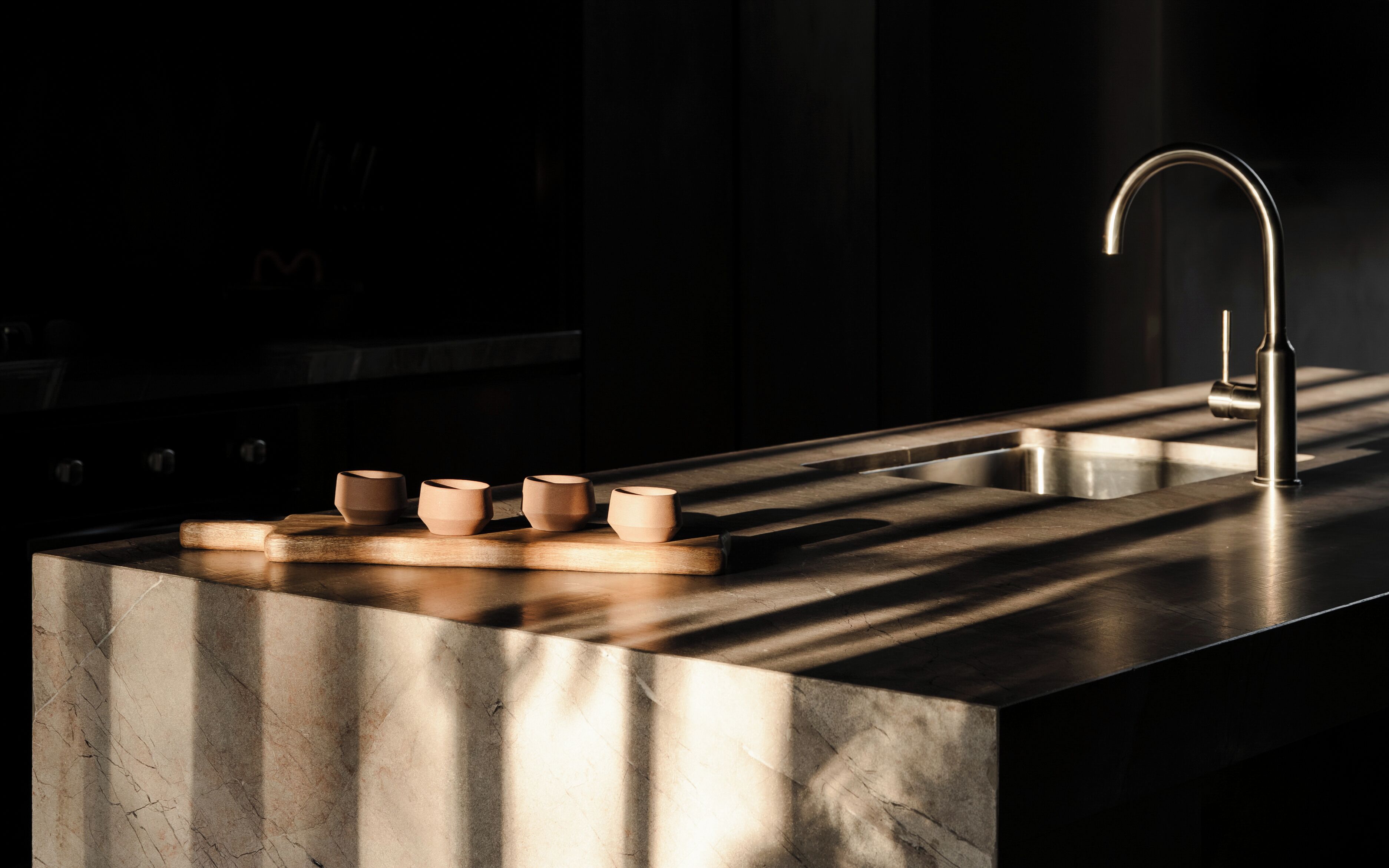 A kitchen with a stainless steel countertop, a modern faucet, and four ceramic cups on a wooden tray.