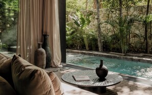 A poolside area with a sofa, two vases, and a book on a round table. - La Reserva Tulum (Tulum)