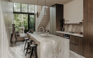 A modern kitchen with a marble countertop, a built-in stove, and a large window overlooking greenery. - La Reserva Tulum (Tulum)