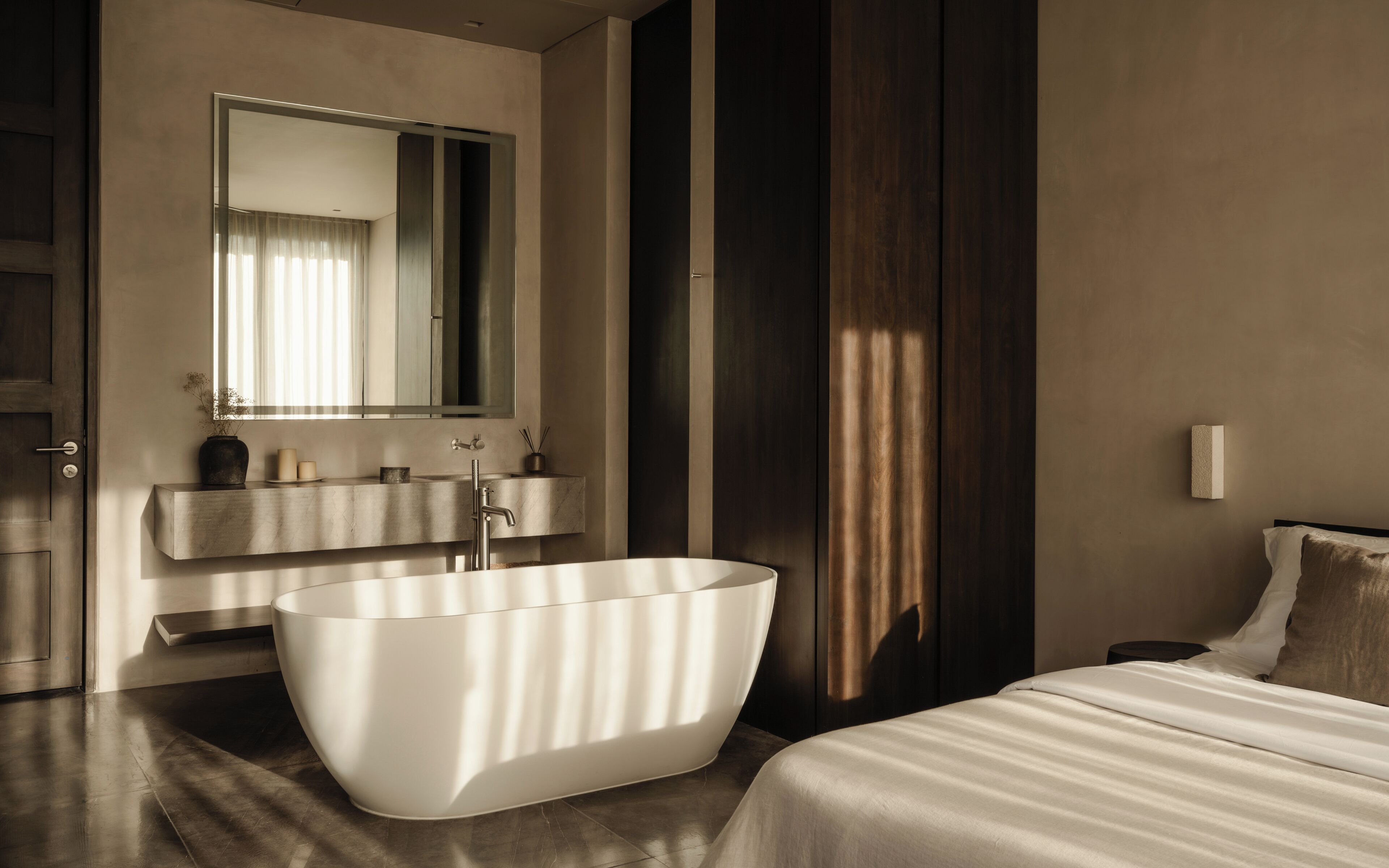 A modern bathroom with a freestanding bathtub, a vanity with a mirror, and a bedside table with a lamp.