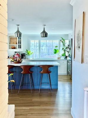 A kitchen with a bar area, wooden flooring, and large windows.