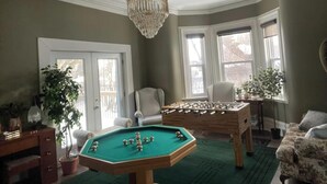 Habitación con mesa de billar, mesa de futbolín, candelabro y dos ventanas con plantas.