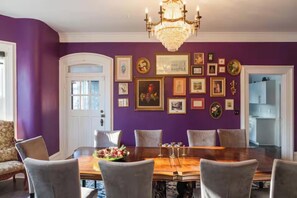 Ein Esszimmer mit violetter Wand, einer Kristallleuchtre und gerahmten Bildern.