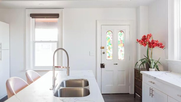 Una cocina con encimera de mármol, pileta de acero inoxidable y una puerta blanca con vidrieras.