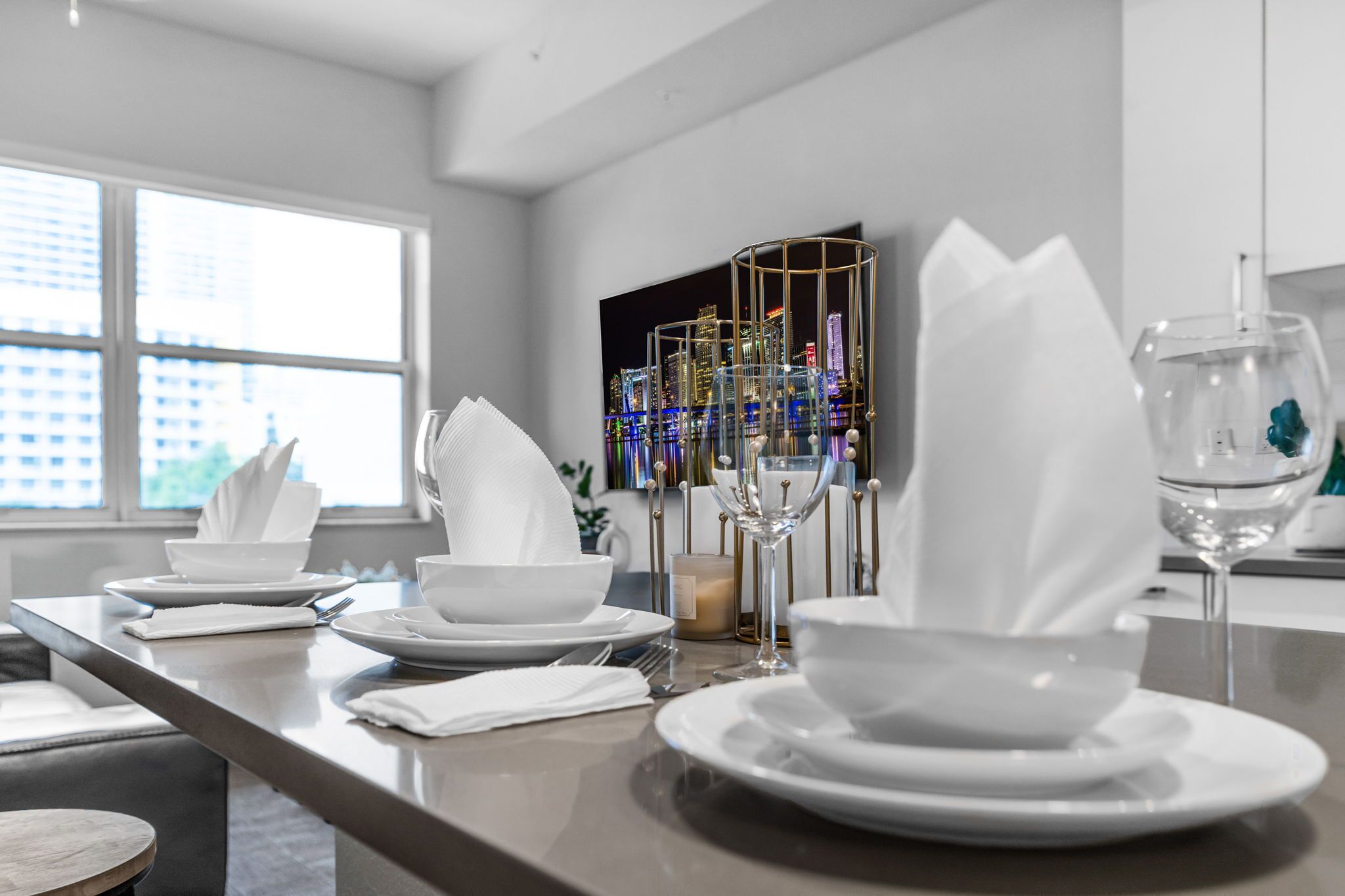Un comedor moderno con vista a la ciudad, un candelabro de vidrio y una decoración de mesa minimalista.