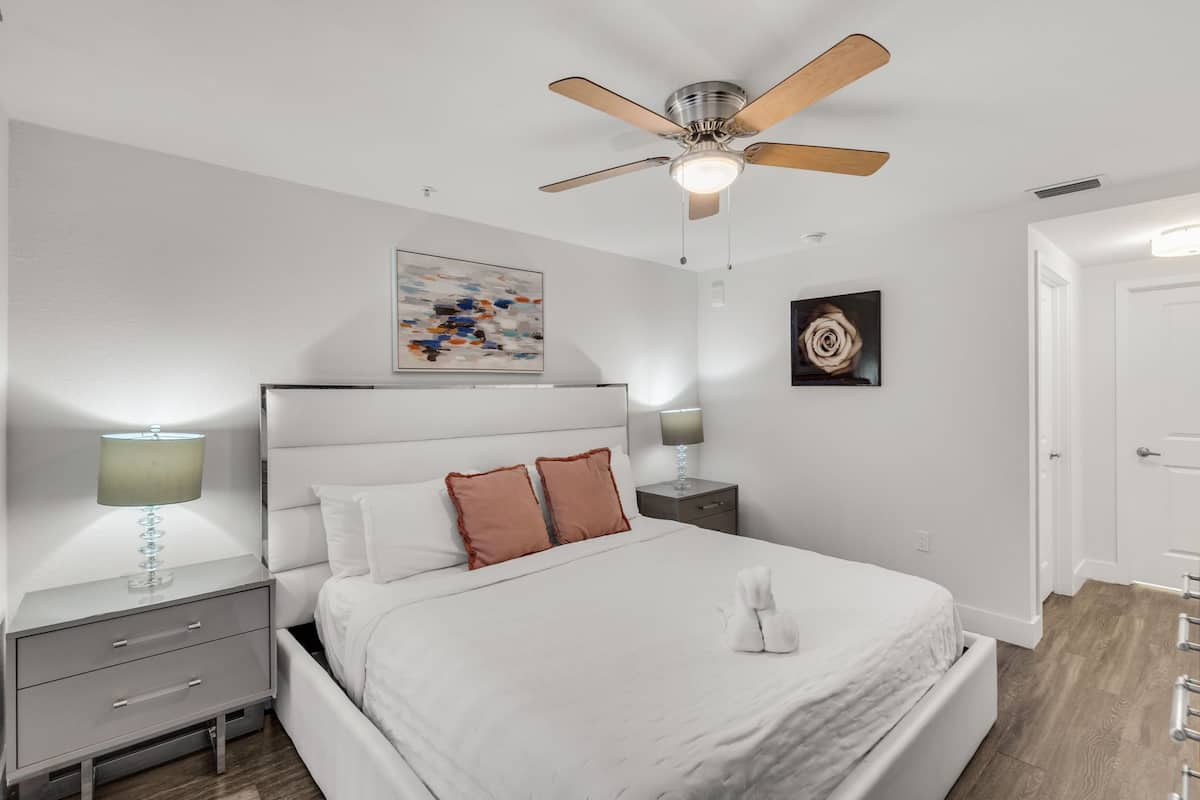 A modern bedroom with a bed, nightstands, a ceiling fan, and artwork on the walls.