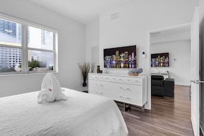 Un dormitorio moderno con una cama grande, un aparador, una televisión y vistas a un horizonte urbano.