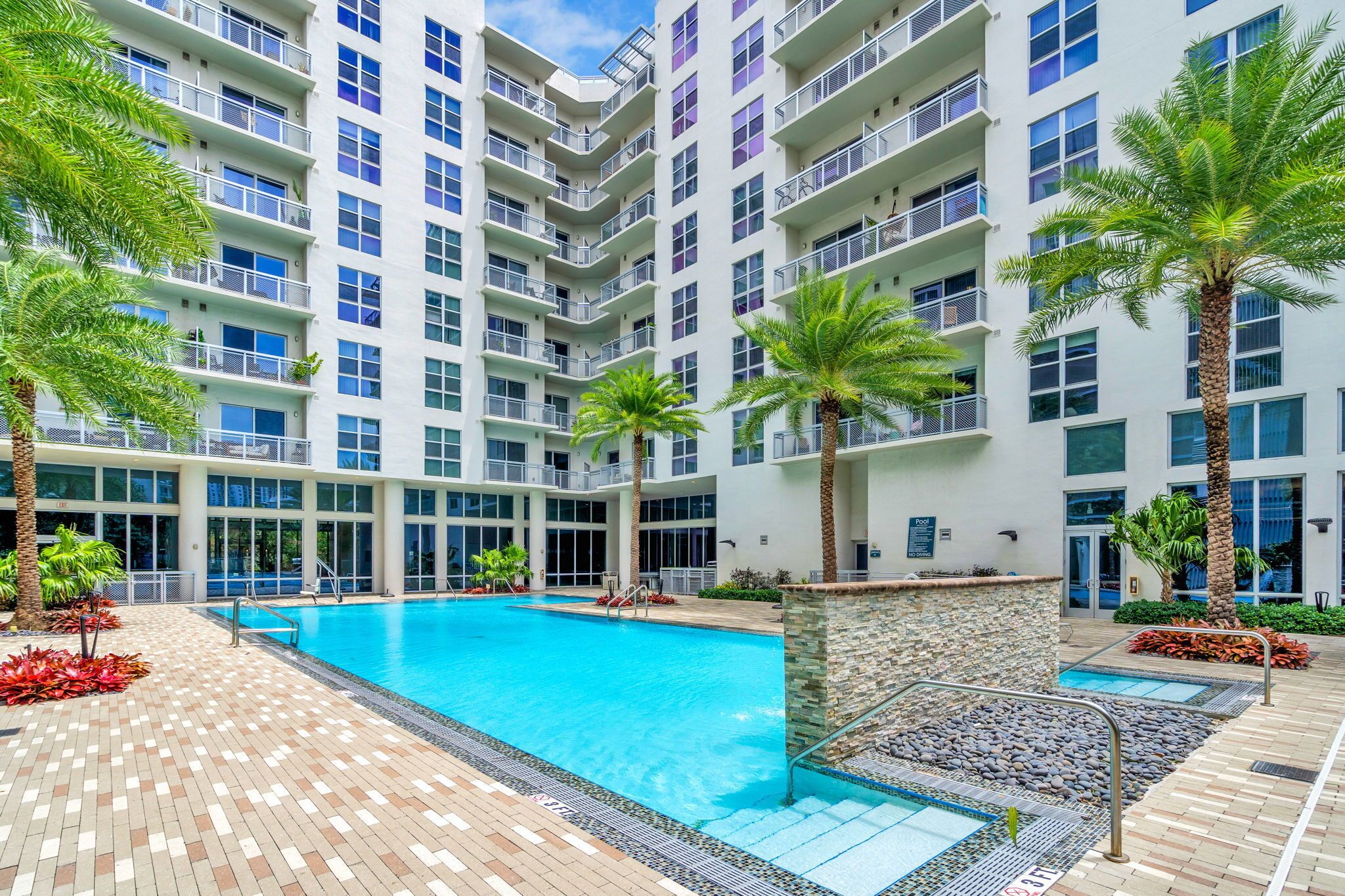 Un hôtel à plusieurs étages doté d’une piscine centrale, de balcons et de palmiers.