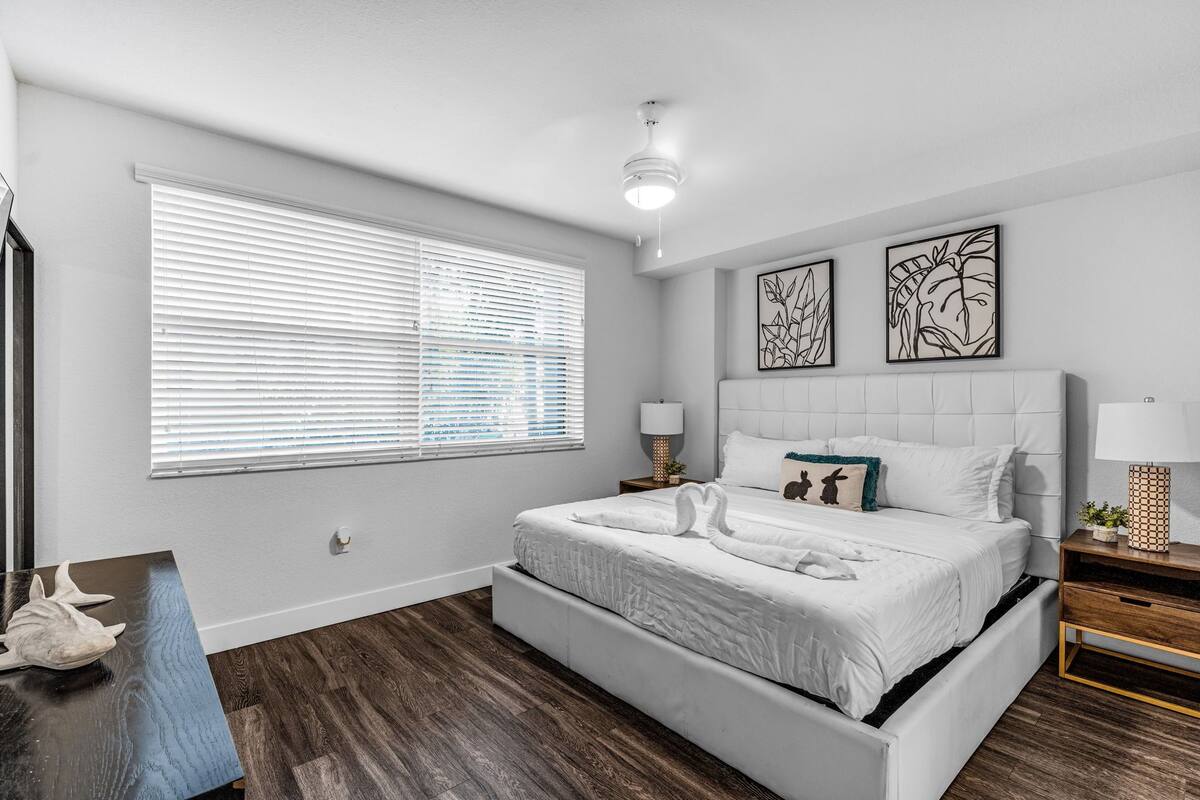 A bedroom with a bed, bedside tables, a window with blinds, and wall art.