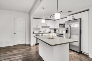 Una cucina moderna con mobili bianchi, un'isola centrale, elettrodomestici in acciaio inossidabile e pavimento in legno.