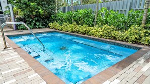 Una piscina rectangular amb un vorejador de rajoles, envoltada per un solàrium de maó i una escala metàl·lica.