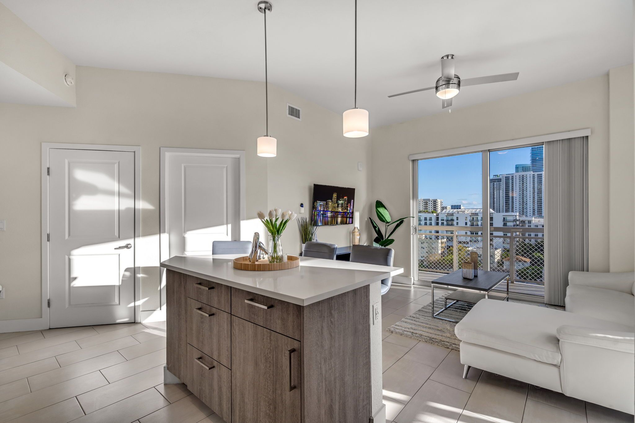 A modern apartment with a kitchen island, dining area, and a balcony with a city view.