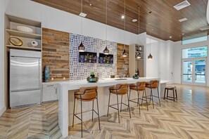 A modern kitchen with a wooden backsplash, a stainless steel refrigerator, and a bar area with stools. - Blu Apartments (Miami)