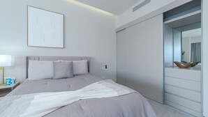 Une chambre à coucher moderne avec un lit, une table de chevet avec une lampe, un grand miroir et un placard à portes coulissantes.