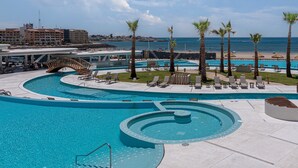 Un complexe hôtelier doté d’une grande piscine, de palmiers et offrant une vue sur l’océan.