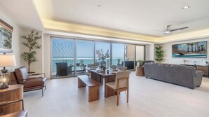 Ein großzügiger Wohnbereich mit Balkon und Meerblick, ein Esstisch für vier Personen und ein graues Sofa.