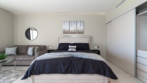 Ein modernes Schlafzimmer mit Bett, einer Couch, einem Spiegel und einem Wandbild.