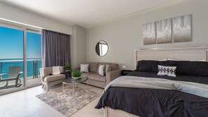 A modern bedroom with a large bed, a sofa, a round coffee table, and a balcony with a view of the ocean. - One 1507c: Sunset Paradise Ocean View (Puerto Peñasco)