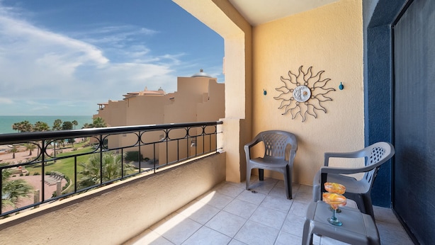 Un balcón con vista a un resort, un adorno de pared y dos sillas de plástico.