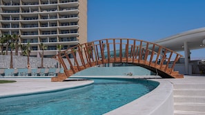 Ein modernes Hotel mit Poolbereich, einer Holzbrücke und einem Hochhaus im Hintergrund.