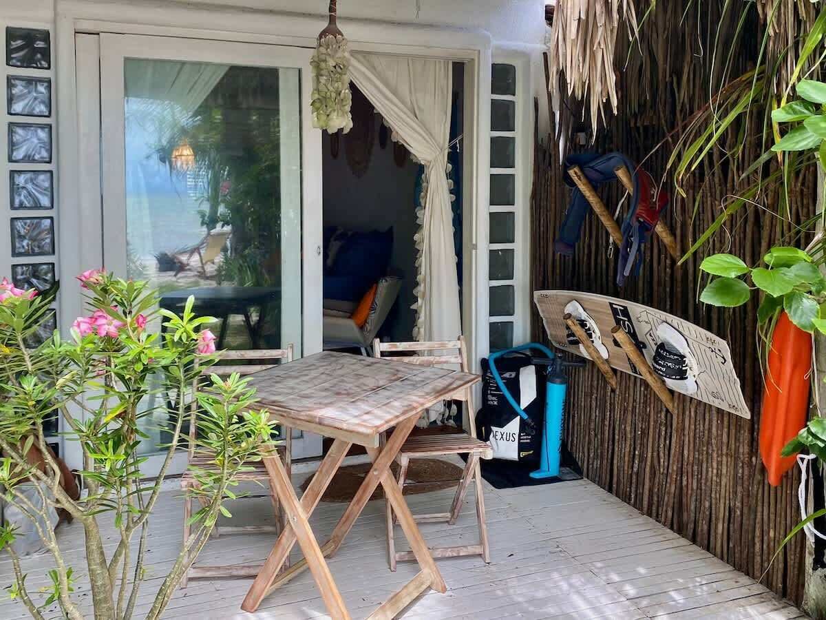 Ein Holztisch mit Stühlen in einer überdachten Außenbereich, verbunden durch eine Schiebetür zu einem Raum.