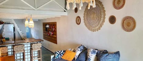 Un espacio de sala acogedor con sofá, una zona de bar con taburetes y una lámpara colgante.