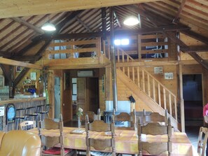 A rustic wooden interior with a dining area, a staircase, and a bar.
