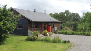 A rustic wooden house with a red door, a chimney, and a gravel driveway.