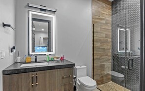 A modern bathroom with a large mirror, a toilet, and a shower area. - The Desert Light Casita (El Paso)