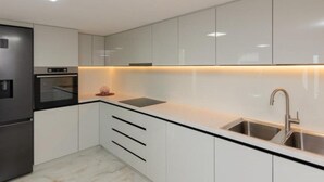 Una cucina moderna con mobili bianchi, un frigorifero nero, forno integrato e lavello in acciaio inossidabile.