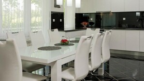 Una cucina moderna con mobili bianchi, un tavolo da pranzo con sedie, lampade a sospensione e vista sull'esterno tramite ampie finestre.