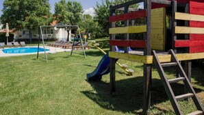 Un'area giochi con scivolo e altalene, una piscina e una casetta colorata di rosso e giallo.