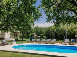 Ein Pool mit Liegestühlen, einer Pergola und einem Steinbau in einem angelegten Garten.