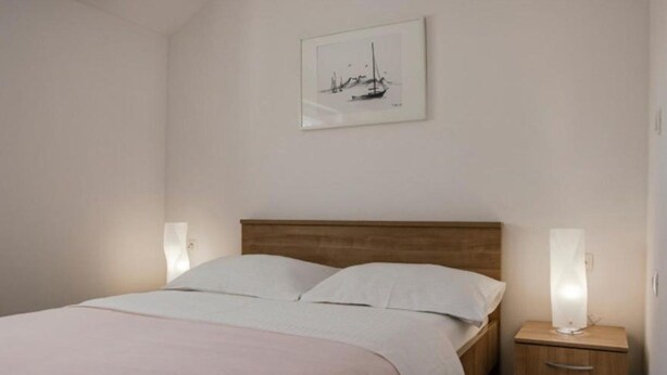 Un letto rifatto con cura, una testiera in legno, un comodino con una lampada e un quadro appeso al muro.