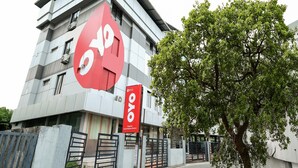 A modern building with a prominent red logo, a tree in front, and a sign indicating a railway station.