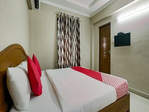 A neatly made bed with a patterned bedspread, a wooden headboard, and two pillows, one white and one red. - Collection O Kadavanthra (Kanayannur)
