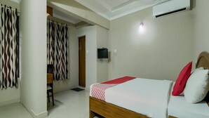 A bedroom with a bed, a ceiling fan, an air conditioning unit, and a television.