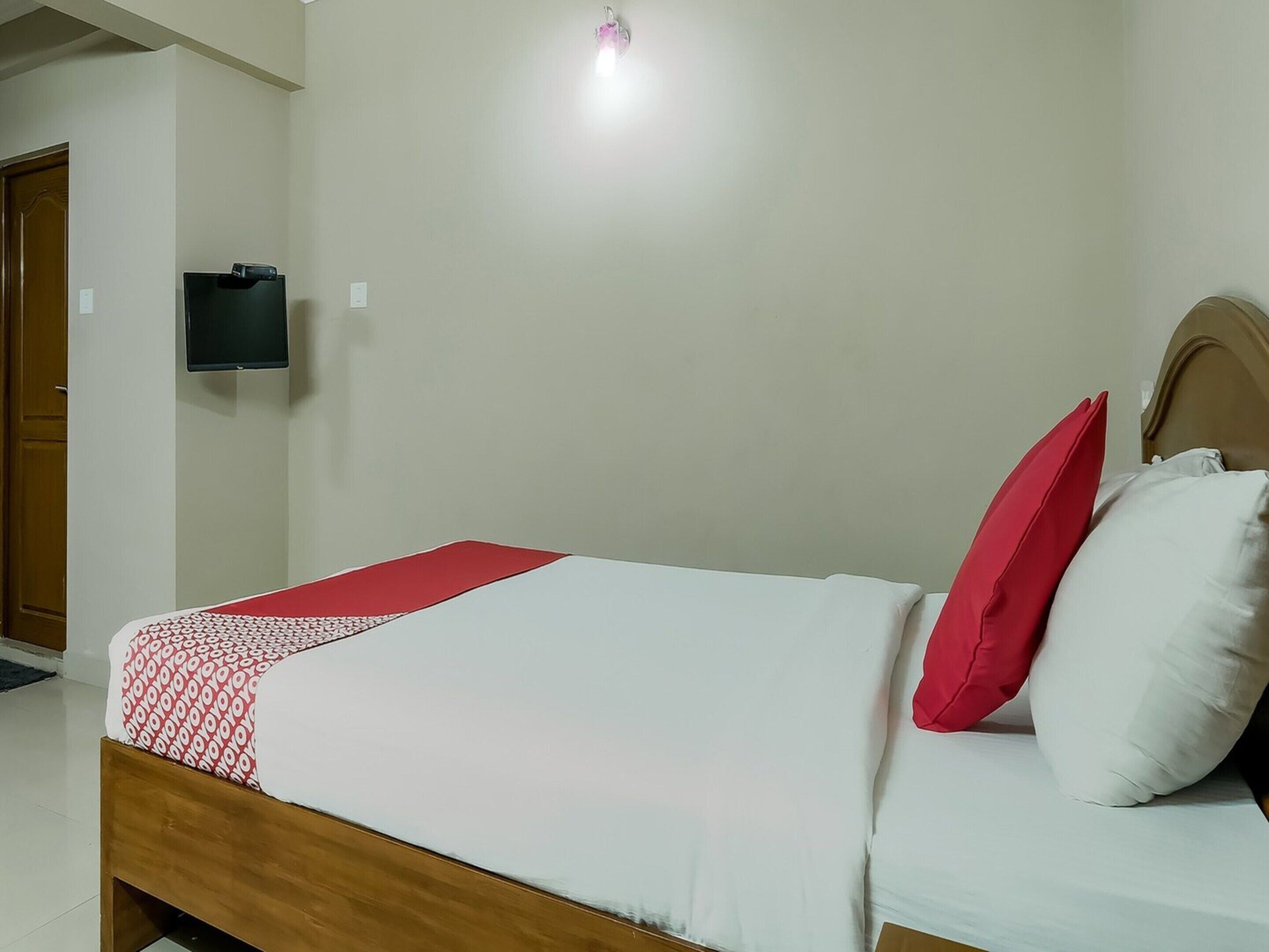 Una cama con una colcha roja y blanca, un cabecero de madera y dos almohadas, una roja y otra blanca.