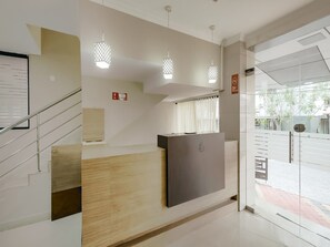 Un comptoir d’accueil avec un plan de travail en bois, un panneau sombre et une porte vitrée donnant sur l’extérieur.