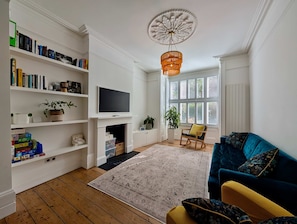 A living room with a TV, bookshelf, sofa, and a large window with blinds. - Chic Property With Backyard Near Emirates Stadium (Greater London)
