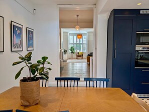 A modern kitchen with a Bosch oven, a dining area with a wooden table and chairs, and a hallway leading to a living space with a large window and a hanging light fixture. - Chic Property With Backyard Near Emirates Stadium (Greater London)